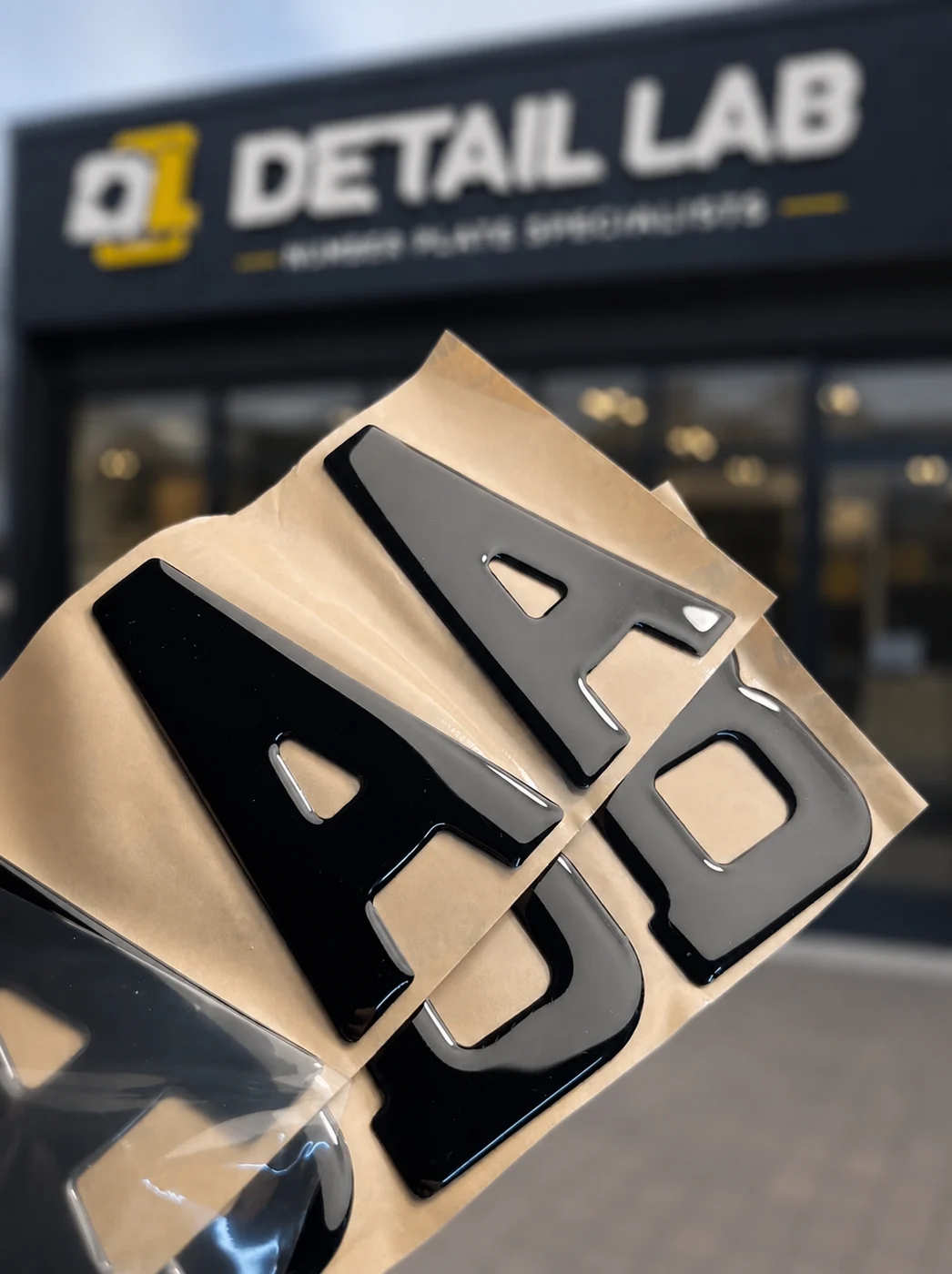 Close-up of gloss black 3D gel plate letters A, A and D on backing paper