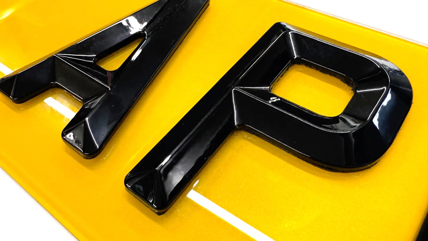 Close-up of bevelled black acrylic plate characters showing the angled edge and flat top face